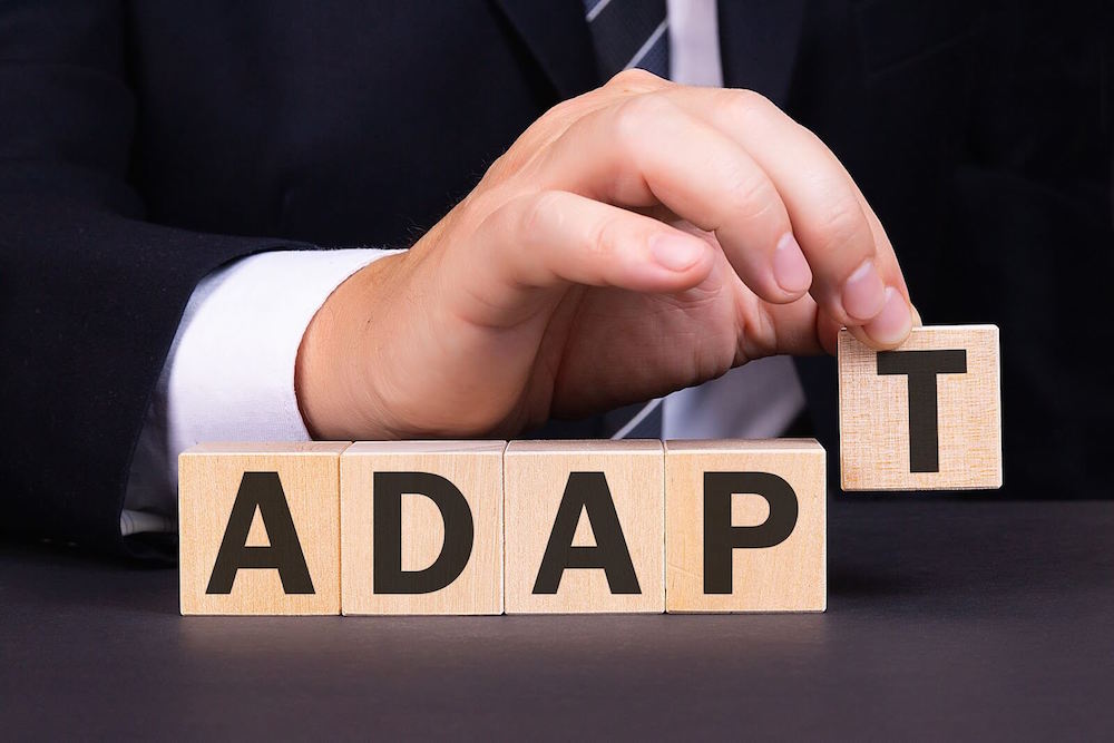 Hand placing block letters together to form the word “Adapt"