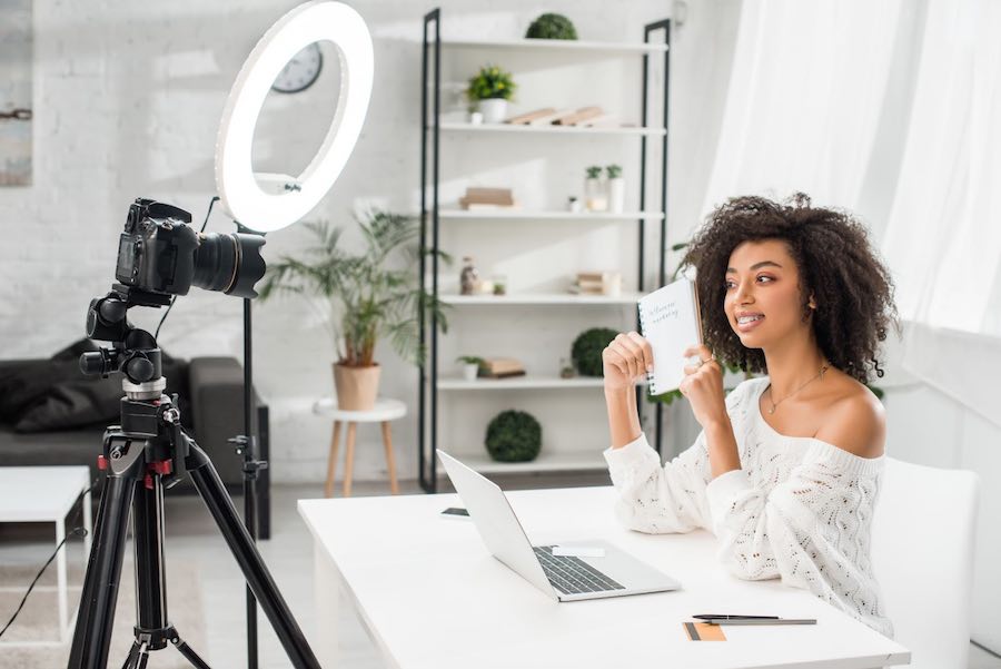 Young black woman creating a video in her home using a circular light bar and camera to promote products. 