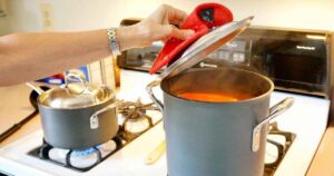 Woman lifts the lid on a large pot of spaghetti sauce.