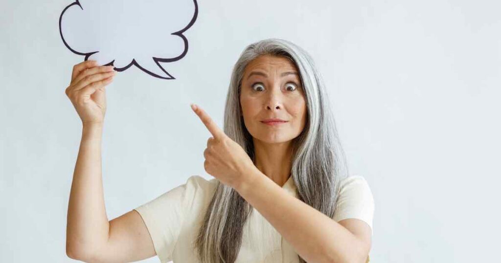 Emotional middle-aged Asian lady points at a blank text bubble.